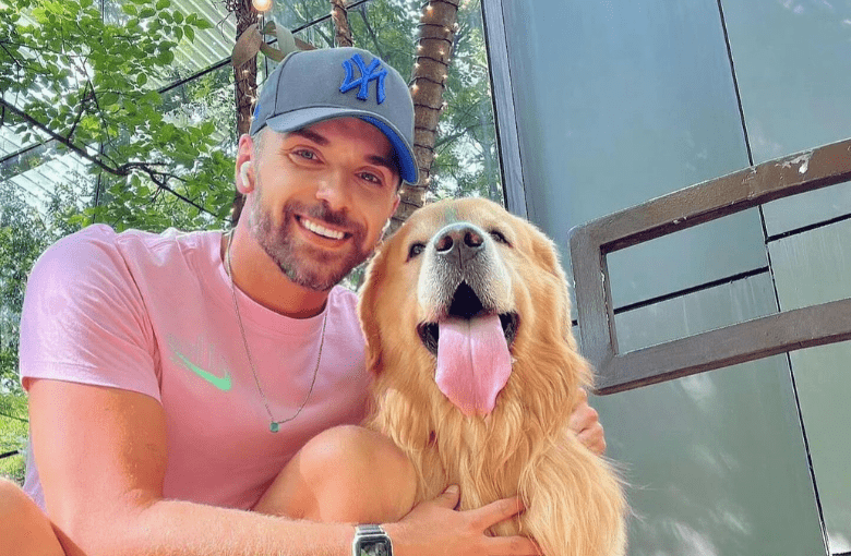 Homem branco de boné azul ao lado de um cão da raça golden retriever